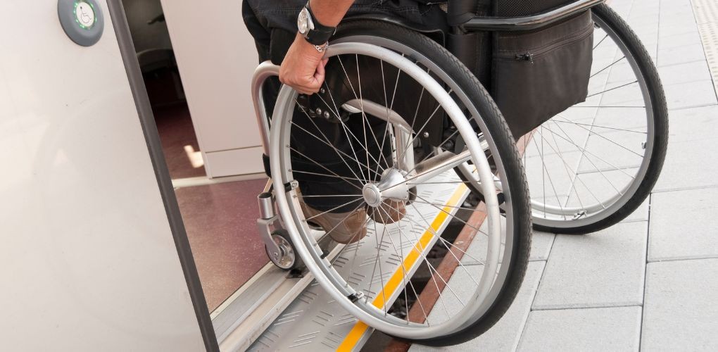 Gros plan sur la main d'une personne sur la roue d'une chaise roulante qui entre dans une voiture de métro.