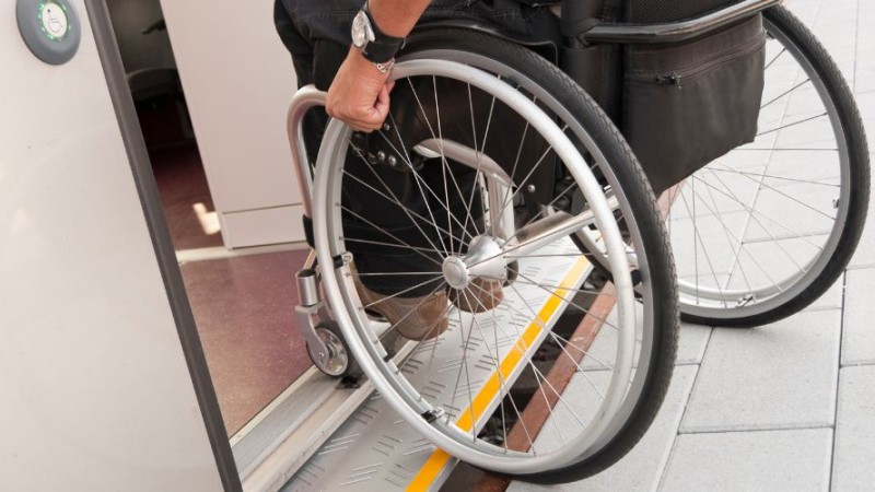Gros plan sur la main d'une personne sur la roue d'une chaise roulante qui entre dans une voiture de métro.