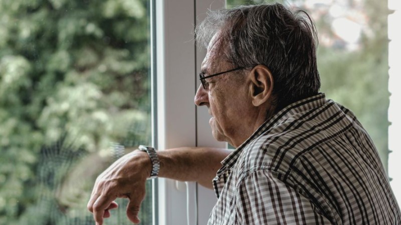 Photographie d'un homme âgé seul regardant par la fenêtre.