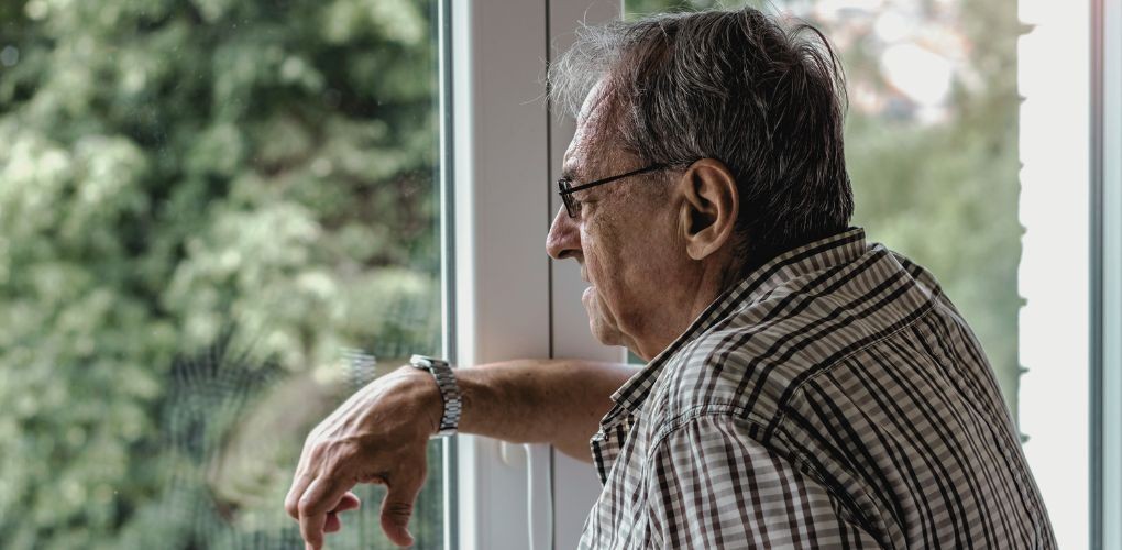 Photographie d'un homme âgé seul regardant par la fenêtre.
